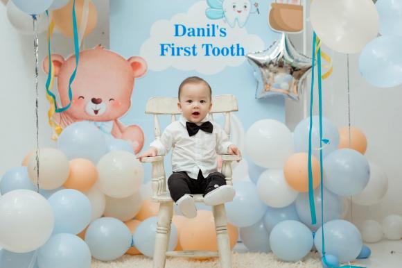 Phía sau là băng rôn với dòng chữ 'Danil’s first tooth'
