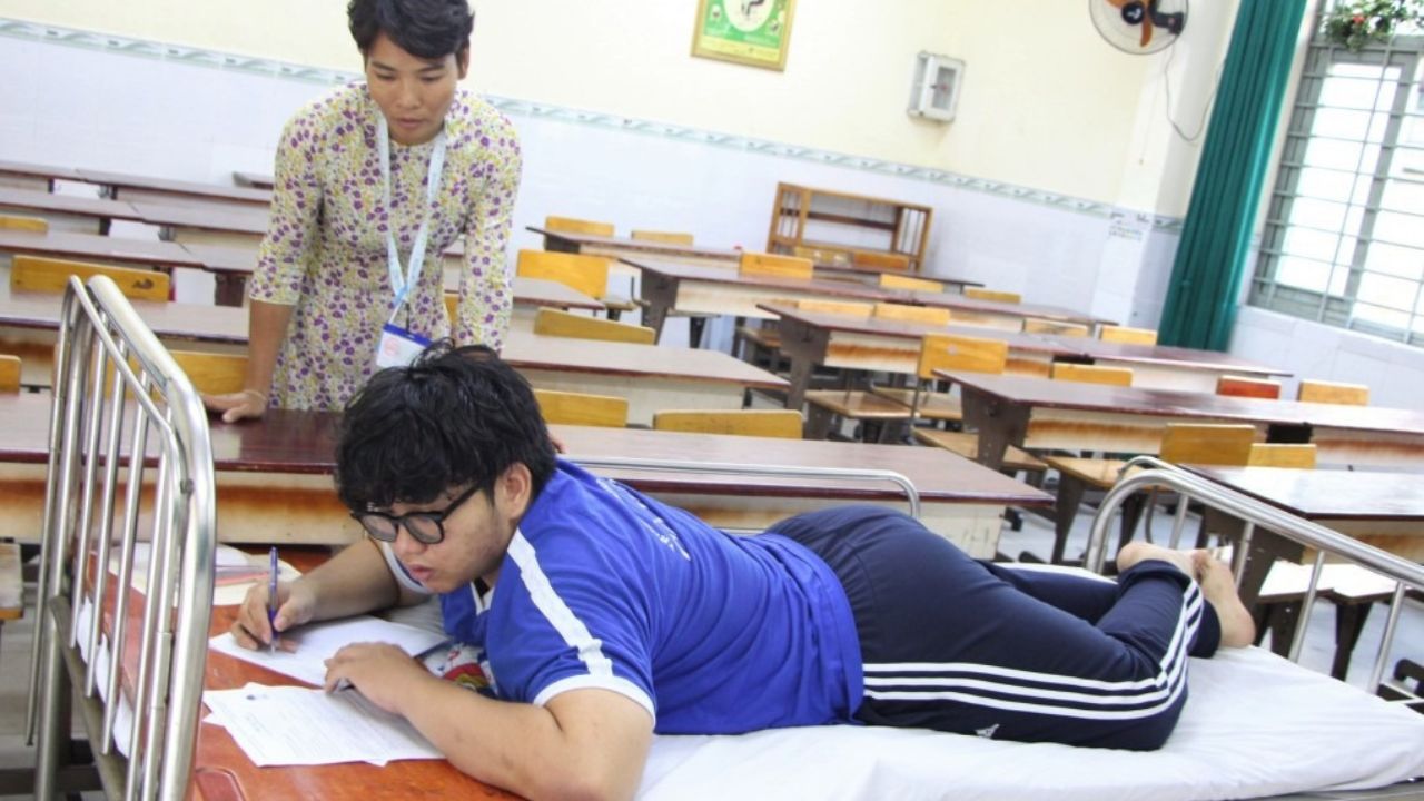 Thí sinh Thiên Phong được hỗ trợ nằm sấp trên giường để hoàn thành bài thi Văn - Ảnh: QT