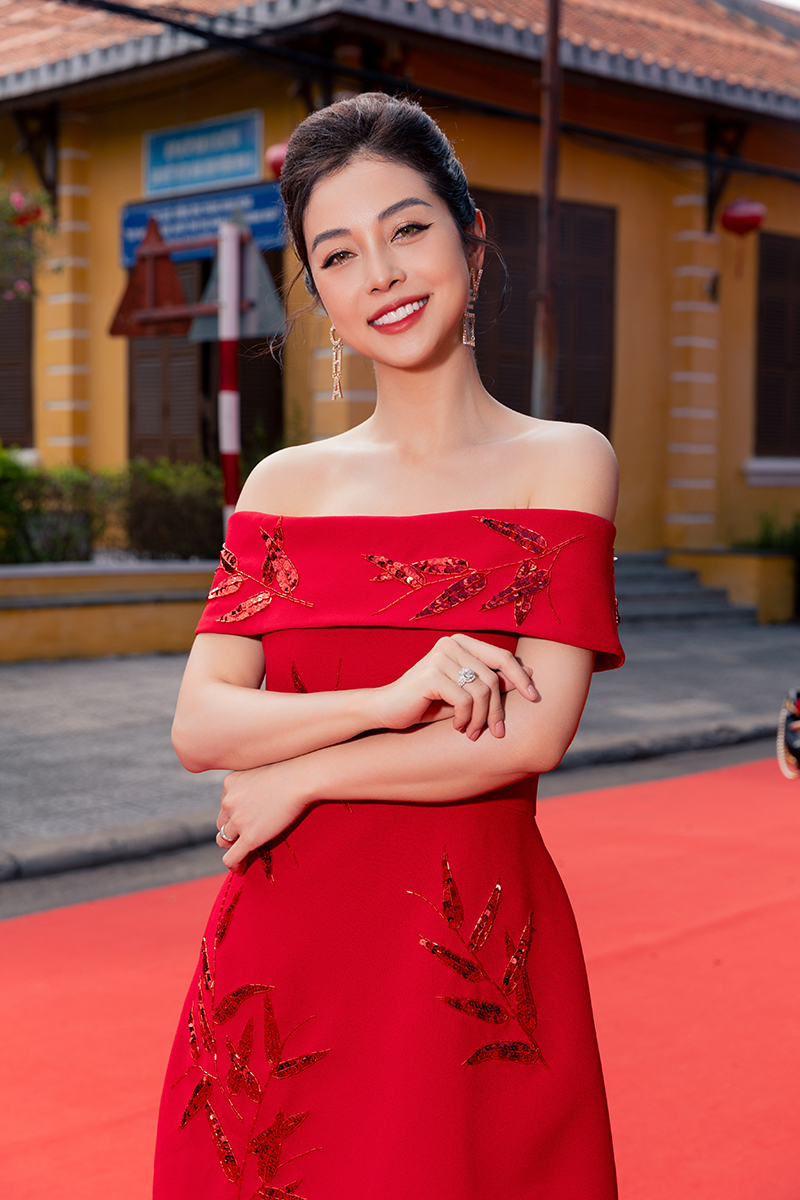 Hoa hậu Jennifer Phạm khoe sắc vóc trẻ trung với thiết kế đầm off shoulder. Hoạ tiết lá tre trên nền sắc đỏ là một trong những thiết kế đinh của BST Cruise 2023 của VUNGOC&SON.
