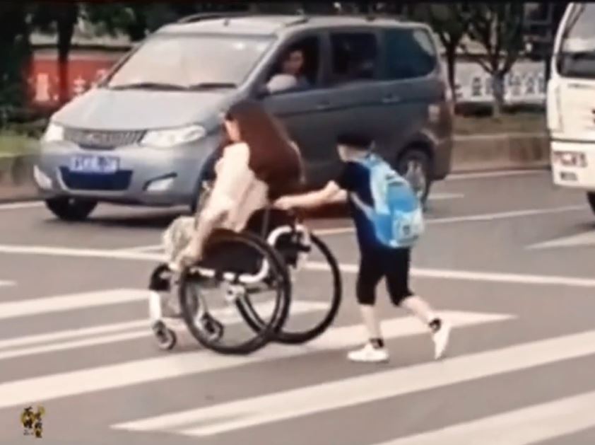 Đoạn clip ghi lại hình ảnh cậu bé đẩy xe lăn giúp mẹ qua đường (ảnh: chụp màn hình)
